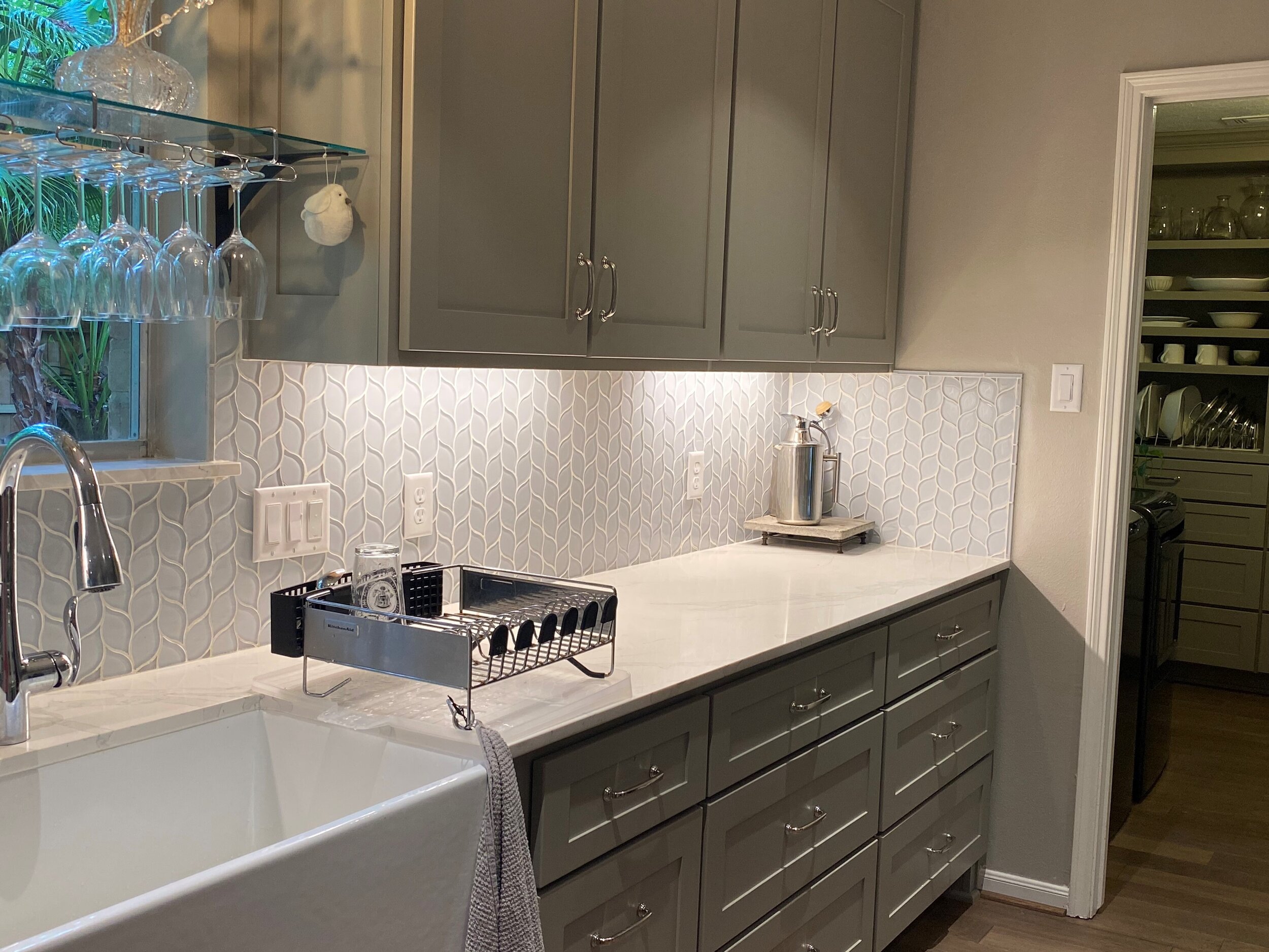 Interior Renovation - Full kitchen remodel with quartz counter top, full height storage in utility, glass tile back splash, under cabinet lighting, flooring, and paint in The Woodlands